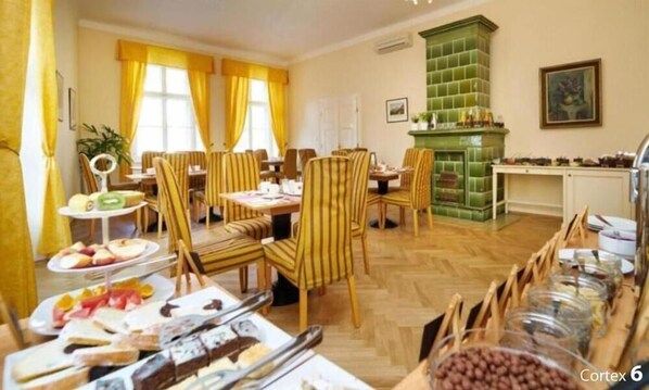 A dining area with striped chairs, a buffet table with various food items, and a green tiled fireplace. - Josephine Old Town Square Hotel - Czech Leading Hotels (Prague)
