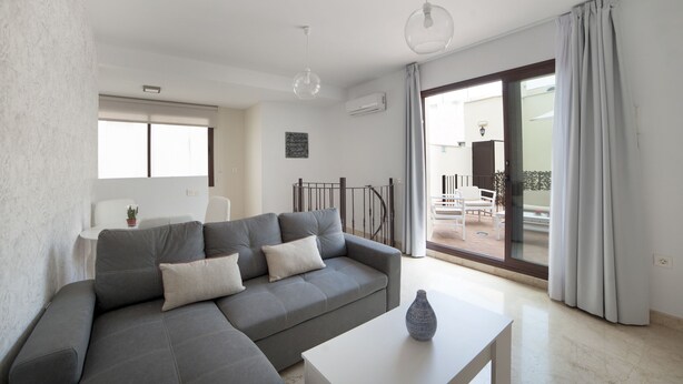 Una sala de estar moderna con un sofá modular gris, una mesa de centro blanca y un ventanal grande.