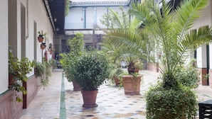 Un patio con macetas, suelo de baldosas y un edificio con tejado de tejas y balcones.