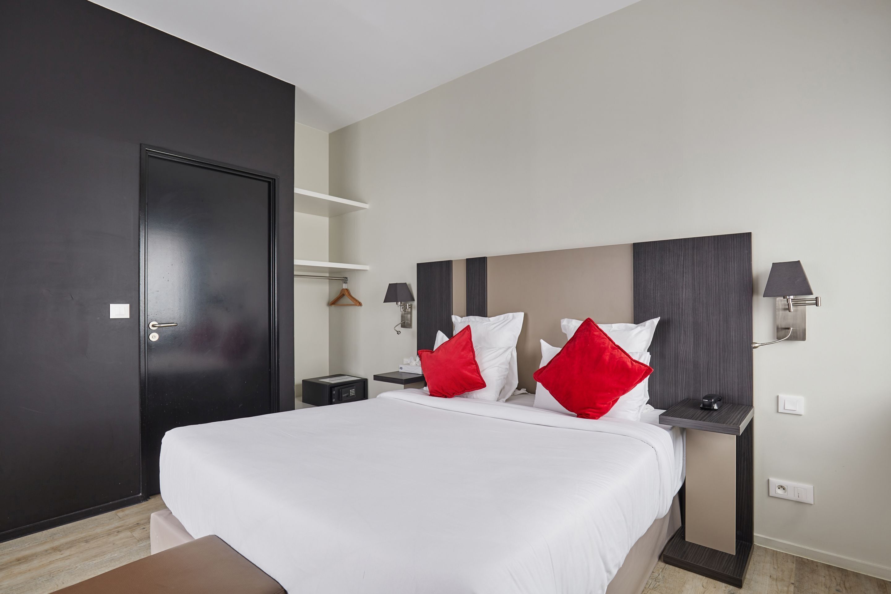 Une chambre d’hôtel avec un grand lit, une porte sombre, une table de chevet avec une lampe et une petite table de nuit.