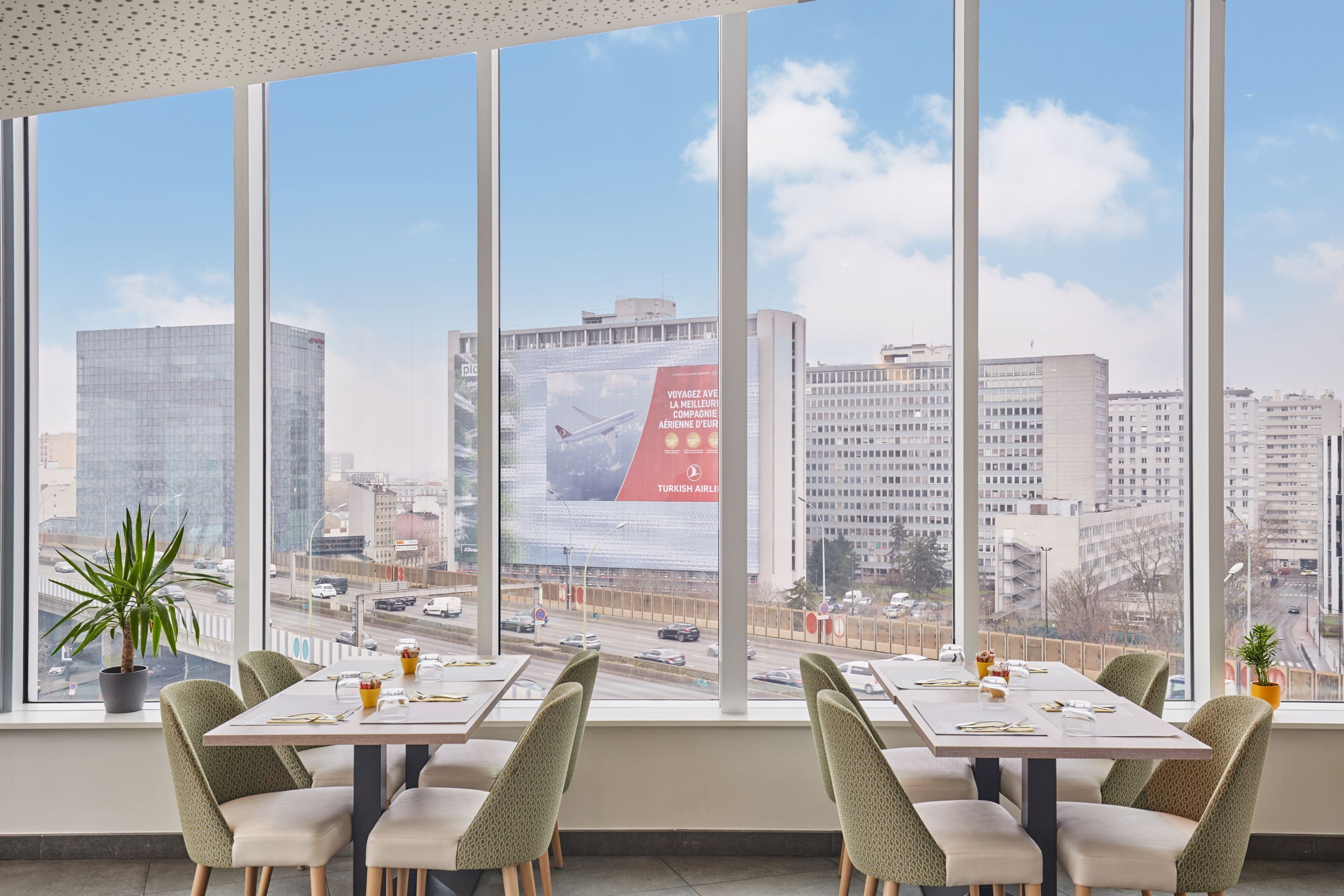A modern dining area with large windows offering a city view, including a prominent billboard.