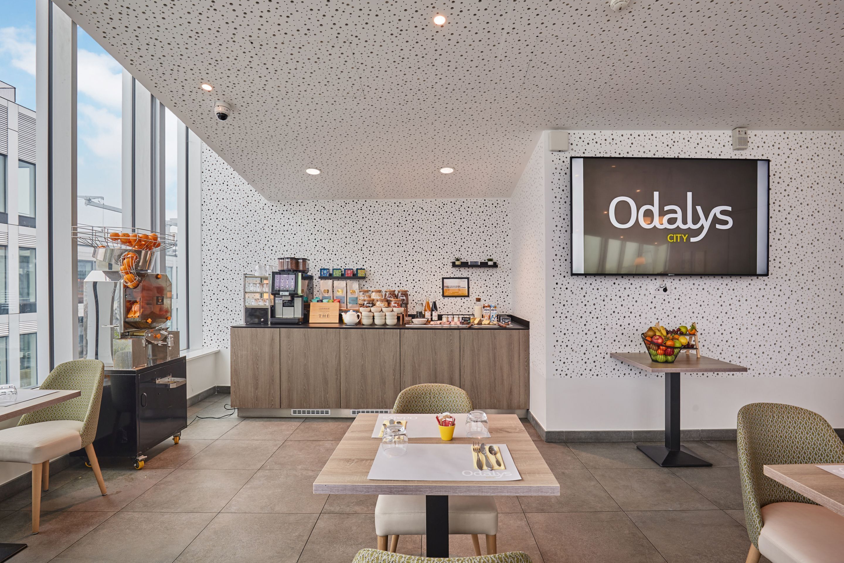 A modern interior with a dining area, a kitchen counter, and a large screen displaying "Odaly's CITY".