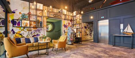 Un hall d’entrée moderne avec un canapé, des fauteuils, une table basse et une bibliothèque remplie de livres et d’objets décoratifs.