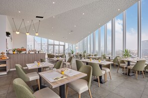 A modern restaurant with high ceilings, large windows, and a city view. - Appart Hotel Odalys City Paris XVII (Paris)