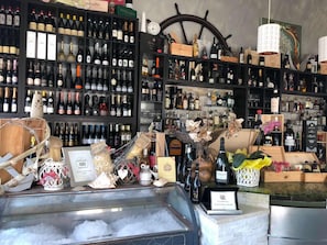 A wine cellar with shelves stocked with various wine bottles, a decorative ship wheel, and a display case with ice and wine accessories. - Ai colli (Teolo)