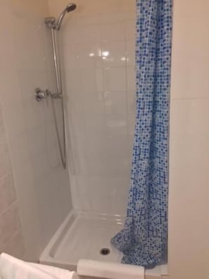 Un espace douche doté d’une porte en verre, d’un pommeau de douche et d’un rideau de douche bleu à motifs.