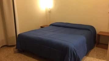 Une chambre à coucher avec un grand lit, une table de chevet, une lampe fixée au mur et un tableau accroché au mur.