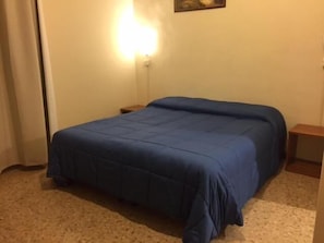 Une chambre à coucher avec un grand lit, une table de chevet, une lampe fixée au mur et un tableau accroché au mur.