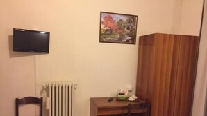 Una habitación pequeña con un escritorio de madera, dos sillas, un radiador, un televisor y un cuadro en la pared.