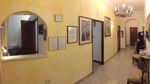 Un pasillo con paredes amarillas, obras de arte enmarcadas, una araña y una puerta que da a otra habitación.