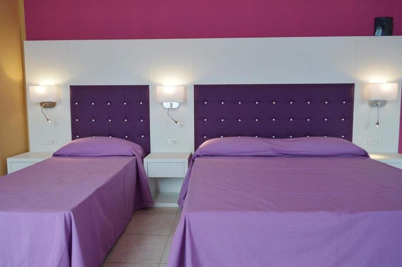 A room with two beds, each with a purple headboard and matching pillows, and bedside lamps.