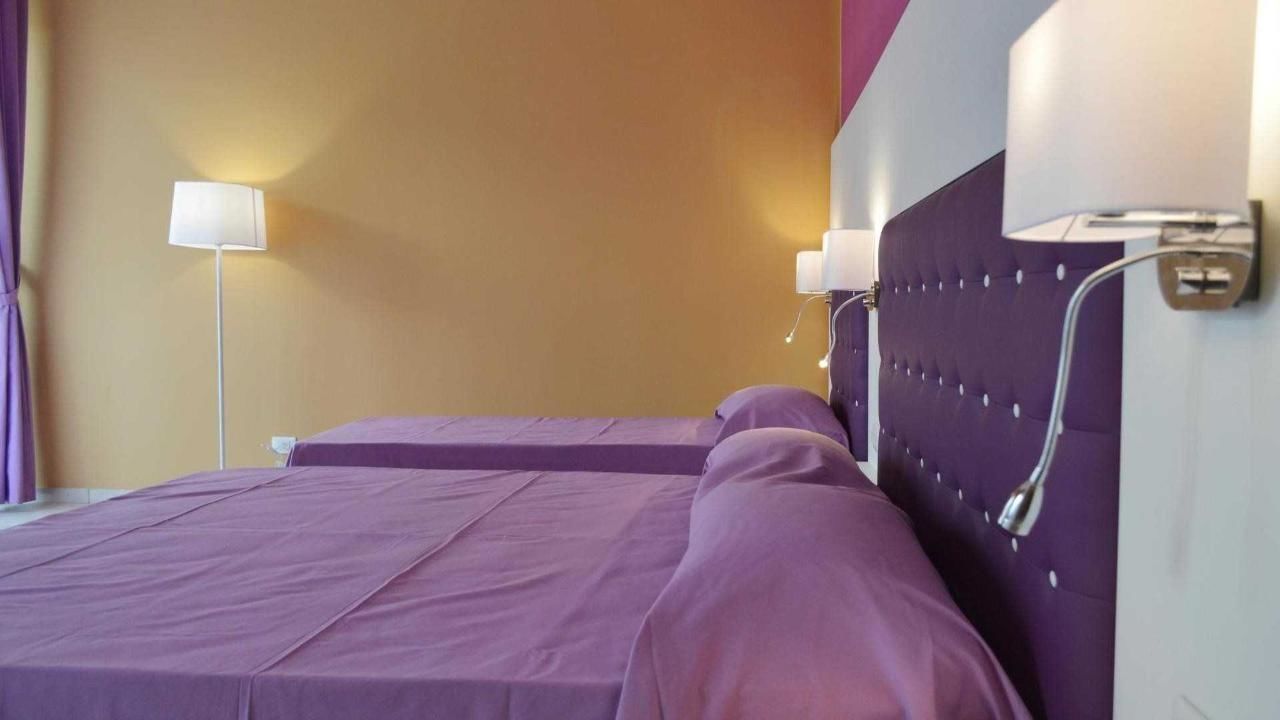A hotel room with a bed, a nightstand, and a wall-mounted lamp.