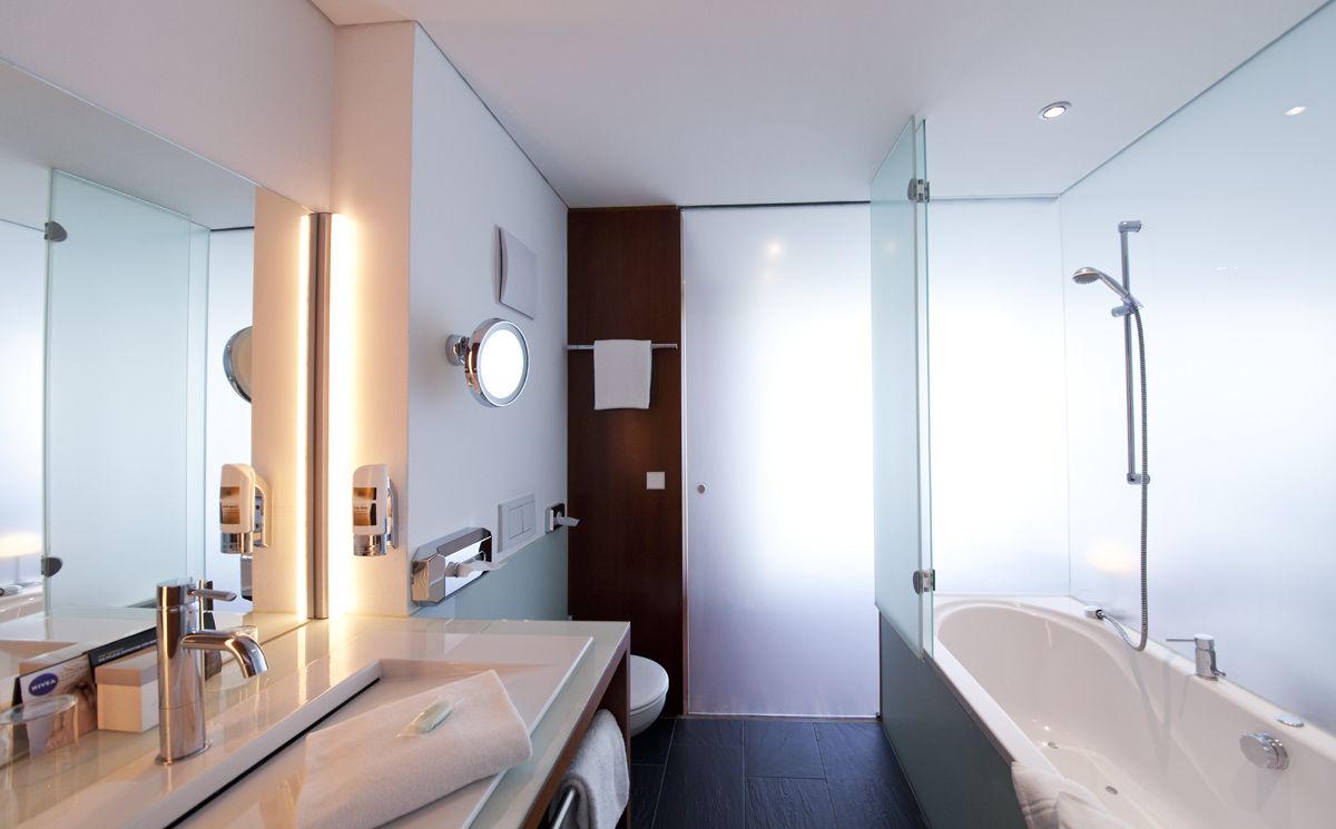 Un baño moderno con un espejo grande, dos lavamanos, una bañera y un box de ducha con paredes de cristal.
