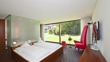 Habitación de hotel moderna con una cama grande, un televisor montado en la pared y vistas al jardín.