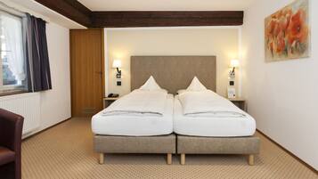 Habitación de hotel con una cama doble, dos mesitas de noche con lámparas, una puerta de madera, una ventana con cortinas y un cuadro en la pared.