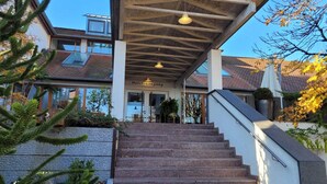 Ein Hotel Eingang mit überdachter Treppe, blauem Himmel und dichter Bepflanzung.