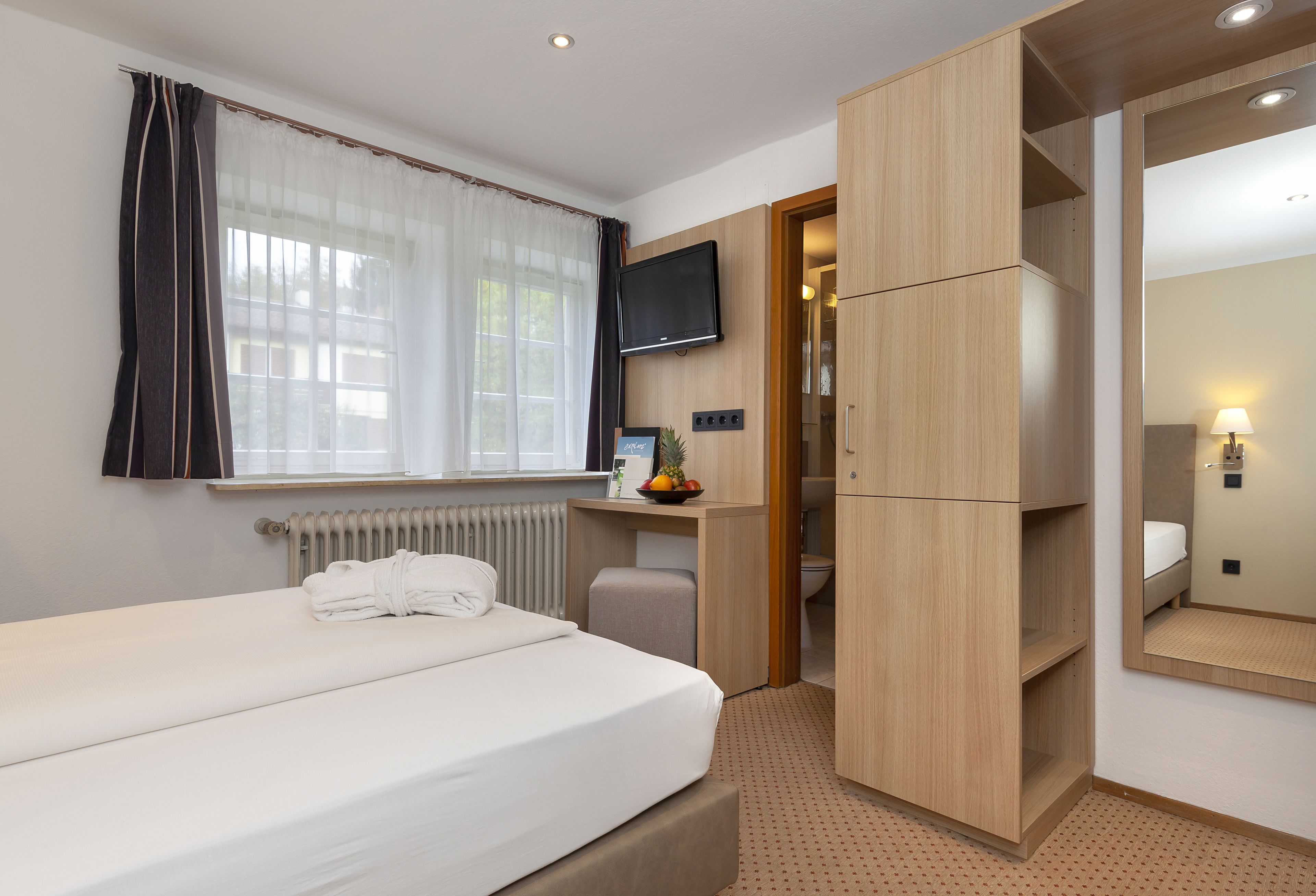 Een hotelkamer met een bed, een bureau, een televisie, een kledingkast en een badkamer.
