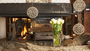 Ein Kamin mit brennendem Holzfeuer, dekorative Hängelampen und eine Vase mit weißen Blumen auf einem Holztisch.