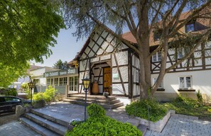 A traditional half-timbered building with a stone staircase leading to the entrance, surrounded by greenery and a parked car. - Romantik Hotel Johanniter-Kreuz (Ueberlingen)