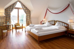 A hotel room with a wooden bed, a round table, a chair, and a view of the outside through large windows. - Romantik Hotel Johanniter-Kreuz (Ueberlingen)