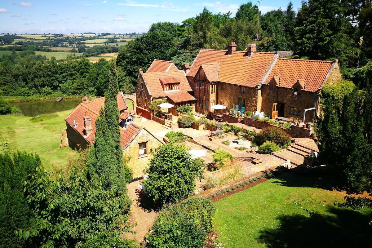 A large stone house with multiple chimneys, surrounded by lush greenery and a well-maintained garden.