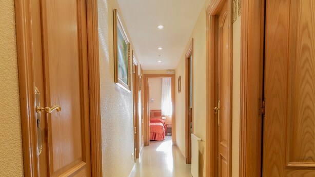 Een hal met houten deuren en een betegelde vloer, die leidt naar een kamer met een bed en een raam.