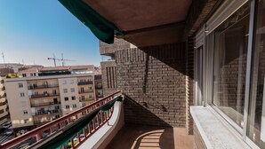Een balkon met een bakstenen muur, een raam en uitzicht op omliggende gebouwen.
