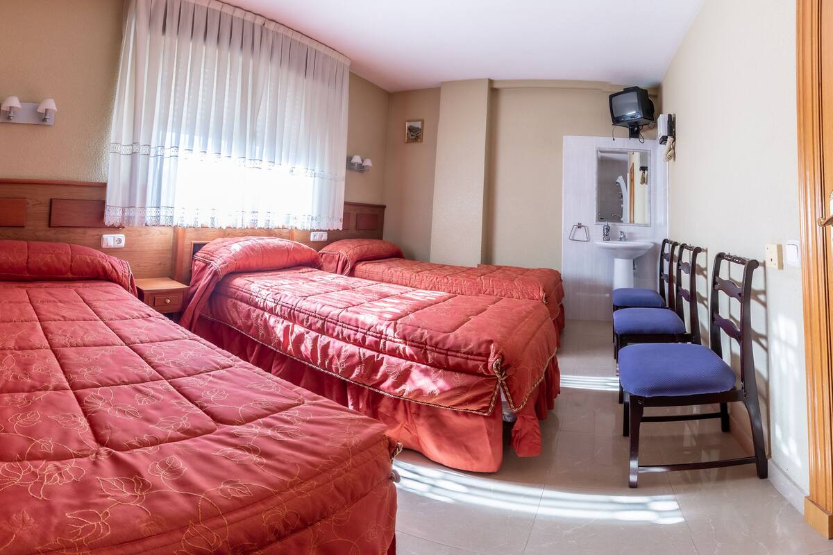 Un dormitorio con tres camas, un escritorio pequeño, una silla y un televisor.