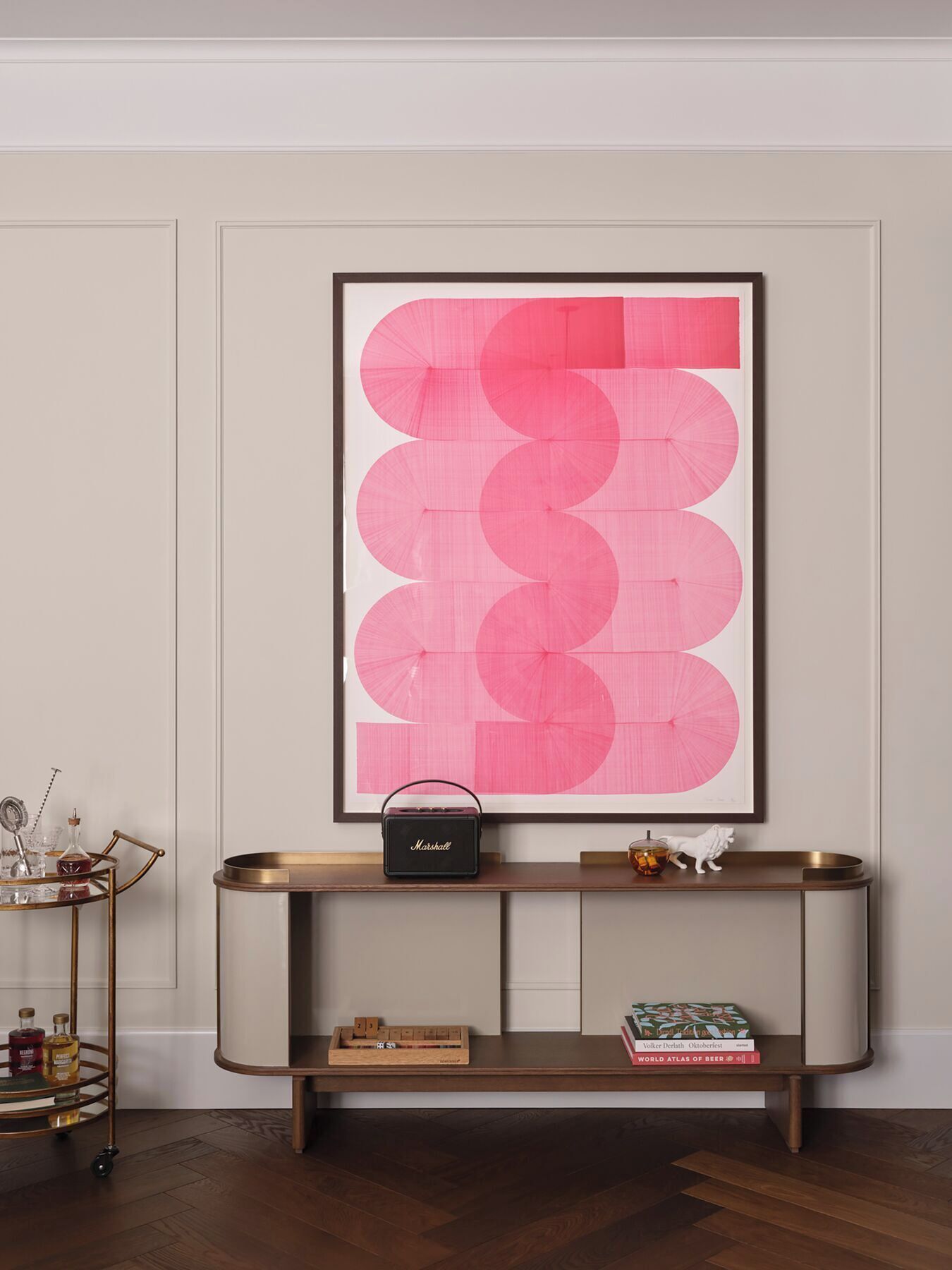 A modern interior with a large abstract artwork, a console table with a radio, and a small shelf with books and decorative items.