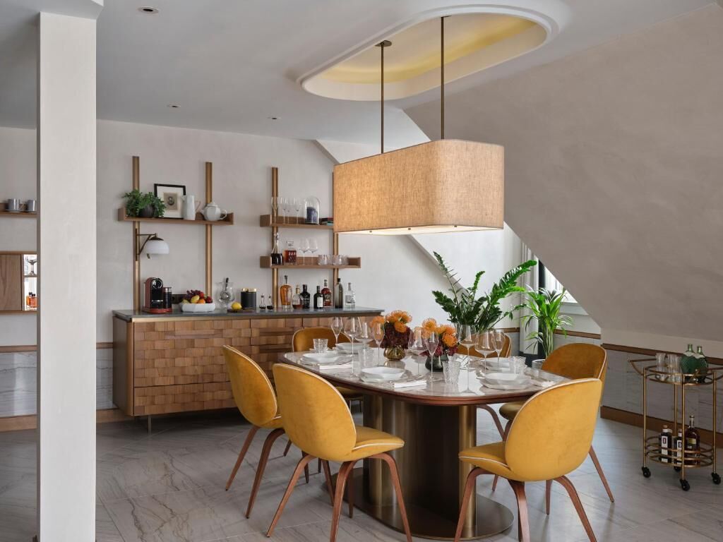 Un comedor moderno con una mesa redonda, sillas amarillas, una lámpara colgante y una cocina al fondo.