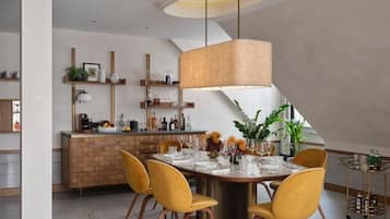 Un comedor moderno con una mesa redonda, sillas amarillas, una lámpara colgante y una cocina al fondo.