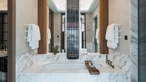 A modern bathroom with a large marble bathtub, wooden accents, and a skylight. - Rosewood Munich (Munich)