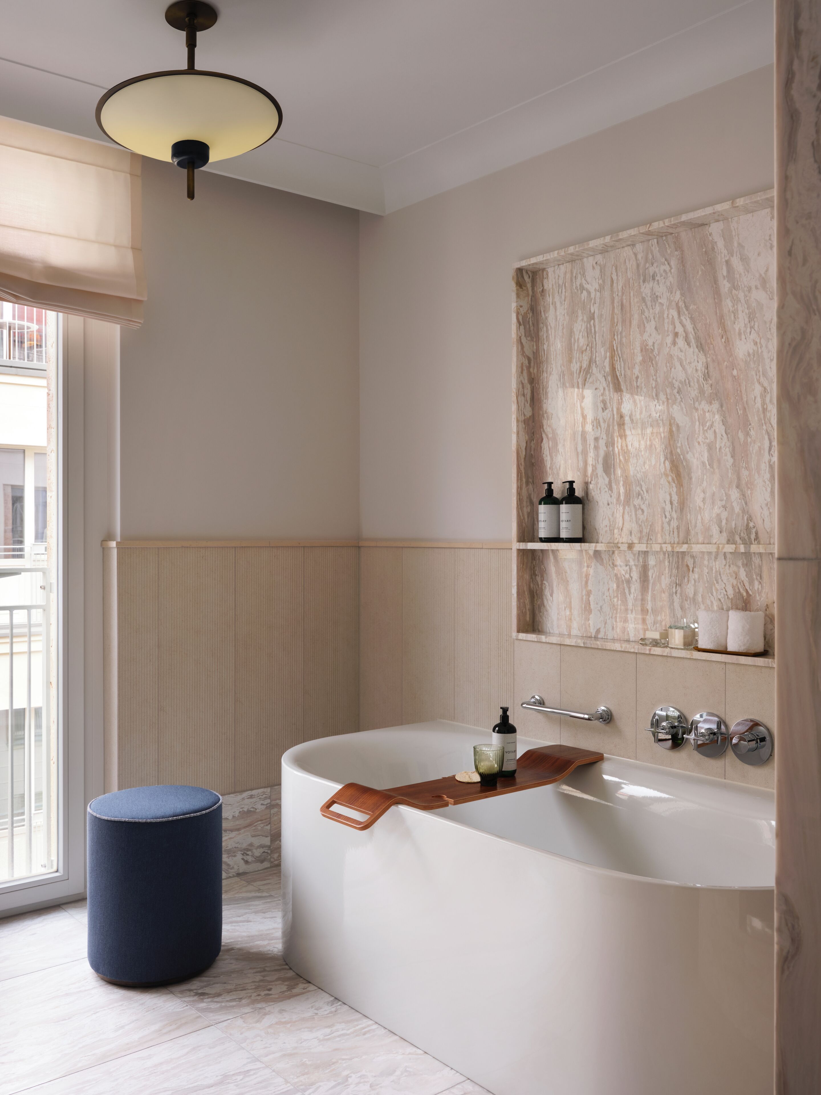 A modern bathroom with a freestanding bathtub, a wooden stool, a towel rack, and a window with a view.