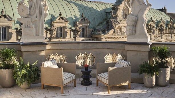 A courtyard with classical statues, a green-roofed building, and outdoor seating with potted plants. - Rosewood Munich (Munich)