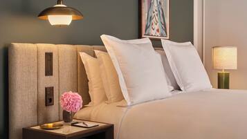 Una cama bien hecha con ropa de cama blanca, una mesita de noche con un florero y una lámpara de pared, además de un cuadro enmarcado sobre la cama.