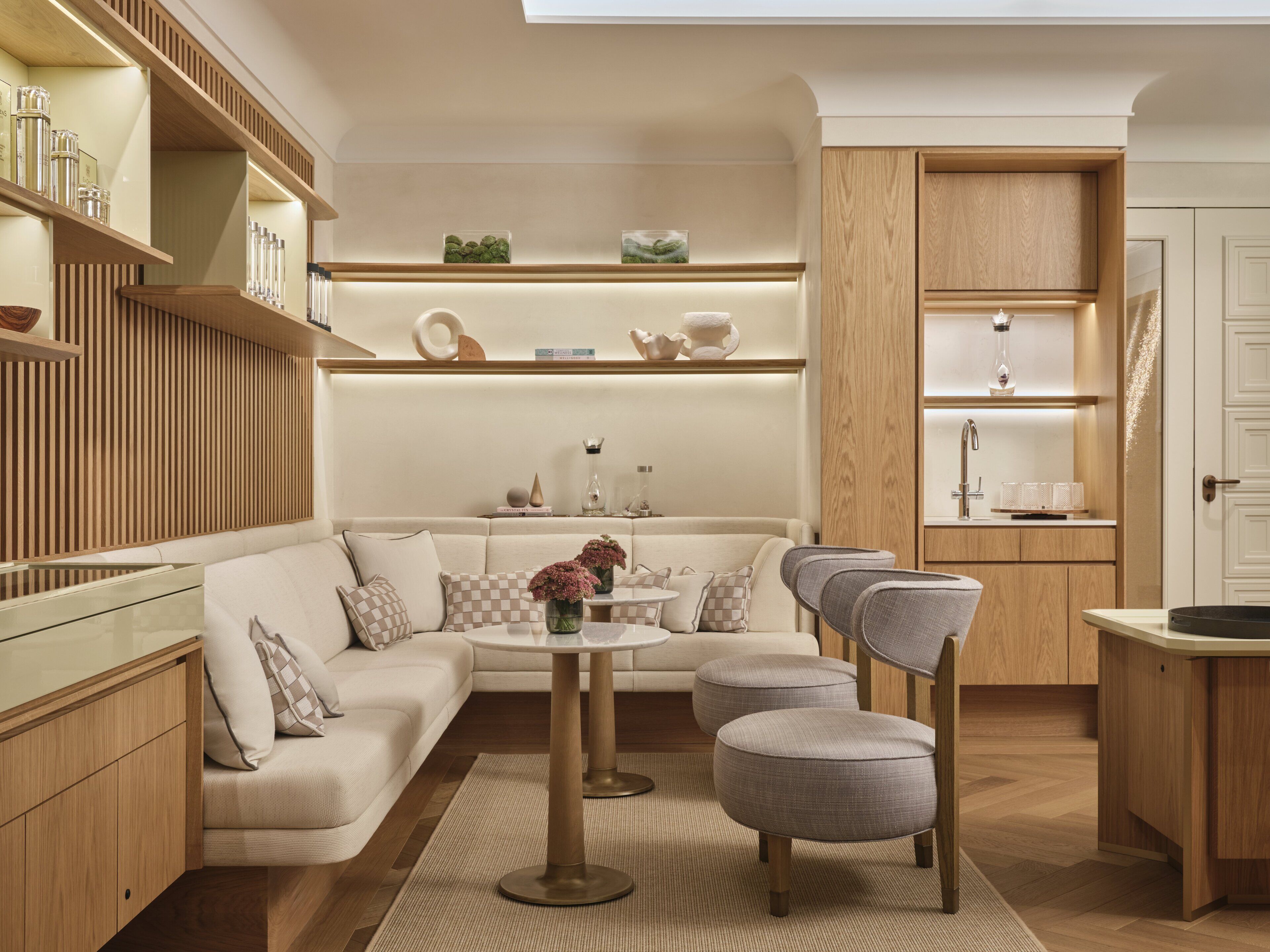 A modern living room with a sofa, ottomans, a coffee table, and a kitchen area with wooden cabinets and a sink.