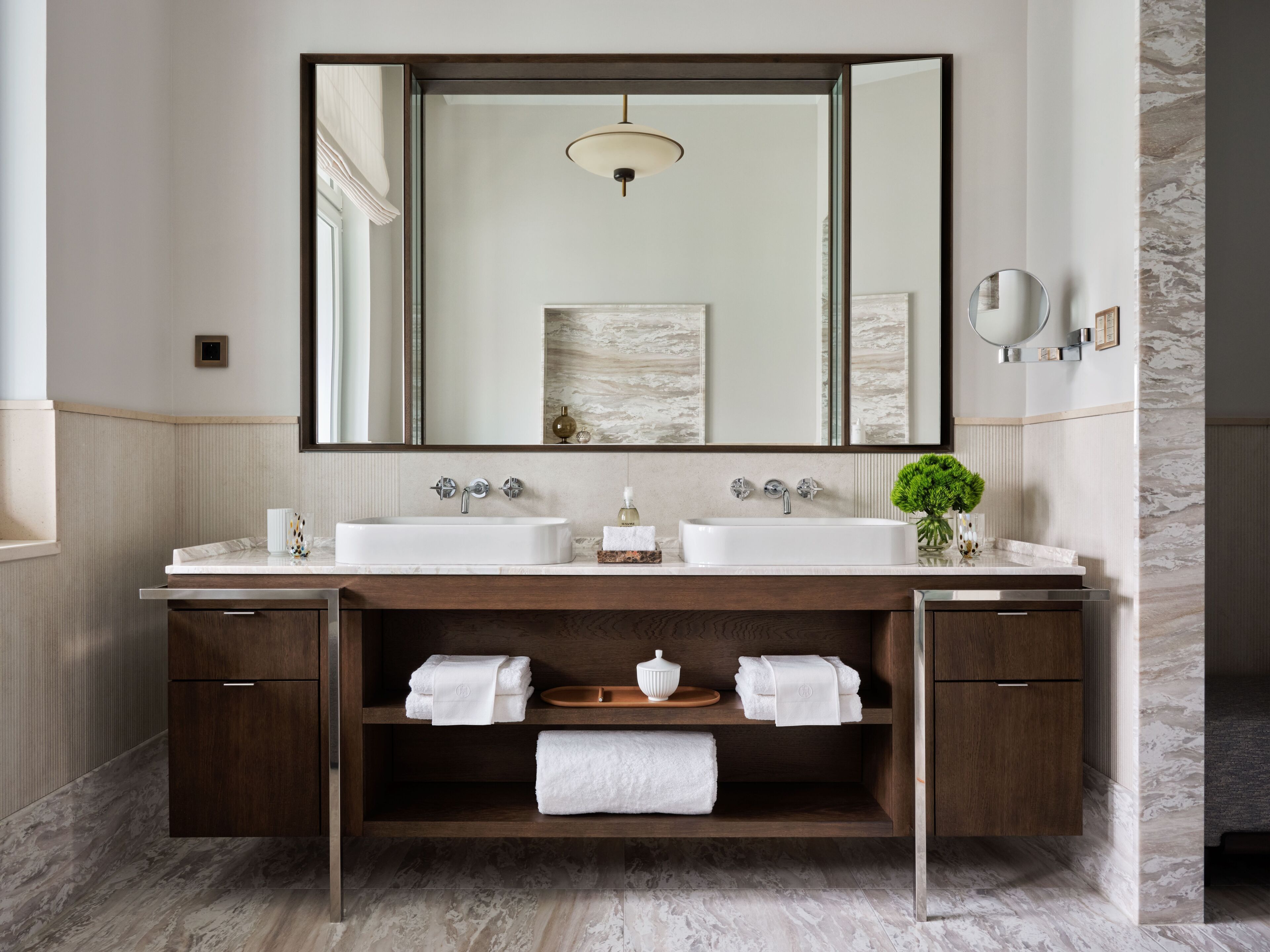 Ein modernes Badezimmer mit zwei Waschbecken, einem großen Spiegel und einem Holzkosmetikschrank mit Regalen für Handtücher.