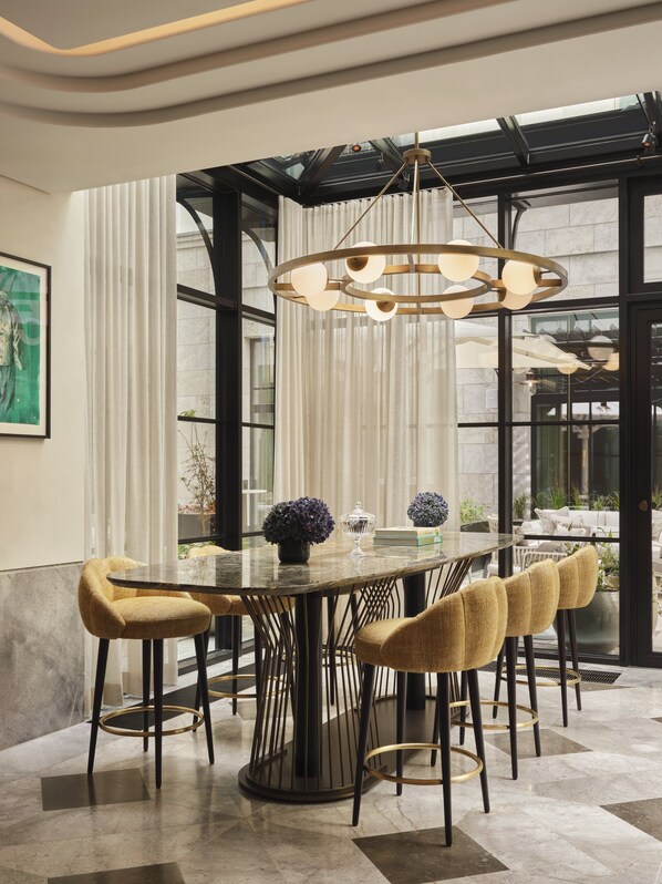 A modern dining area with a glass table, six bar stools, and a unique chandelier.