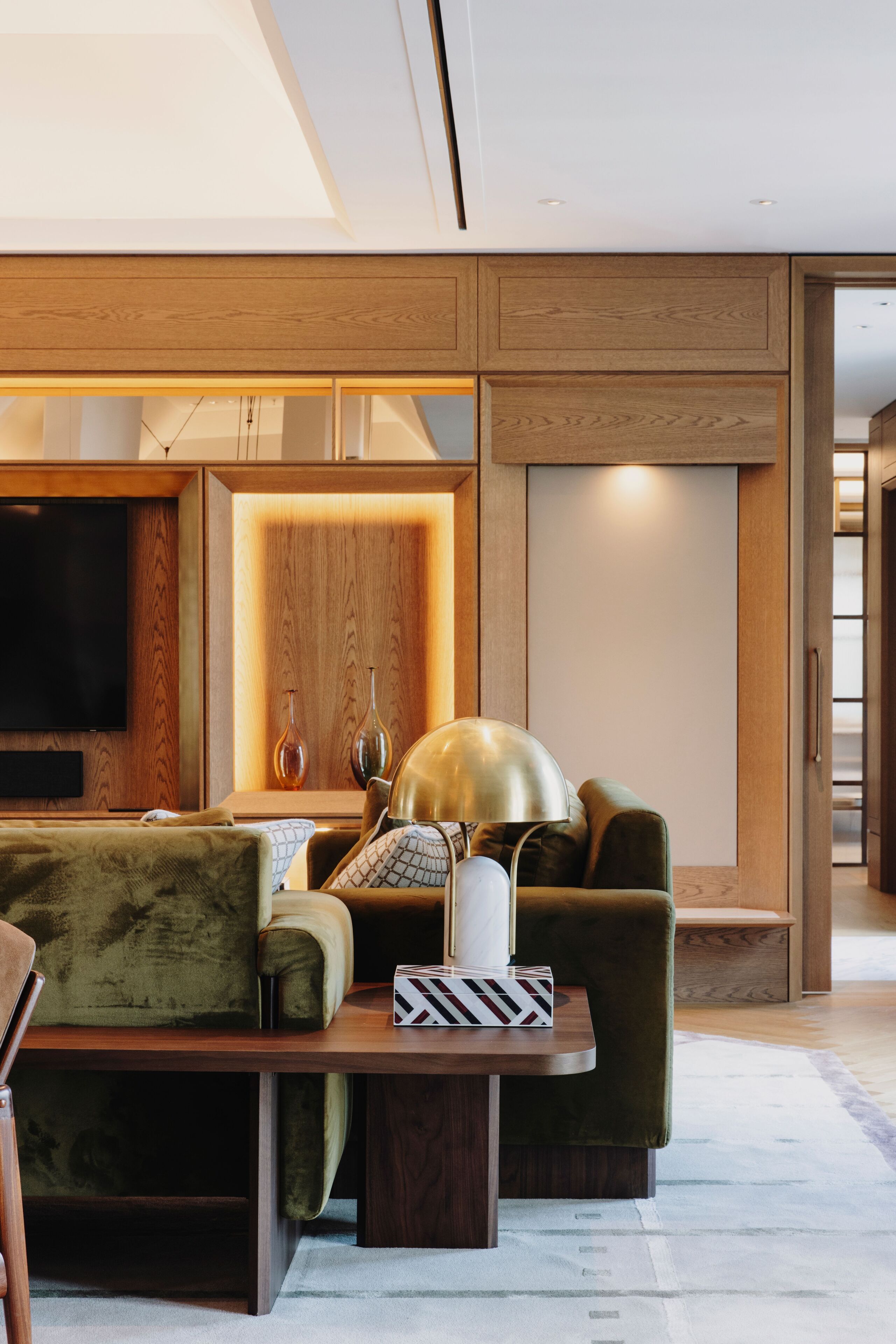 Una sala de estar moderna con una pared de acento de madera, un televisor de pantalla plana, un sofá verde, una mesa de centro y una lámpara.