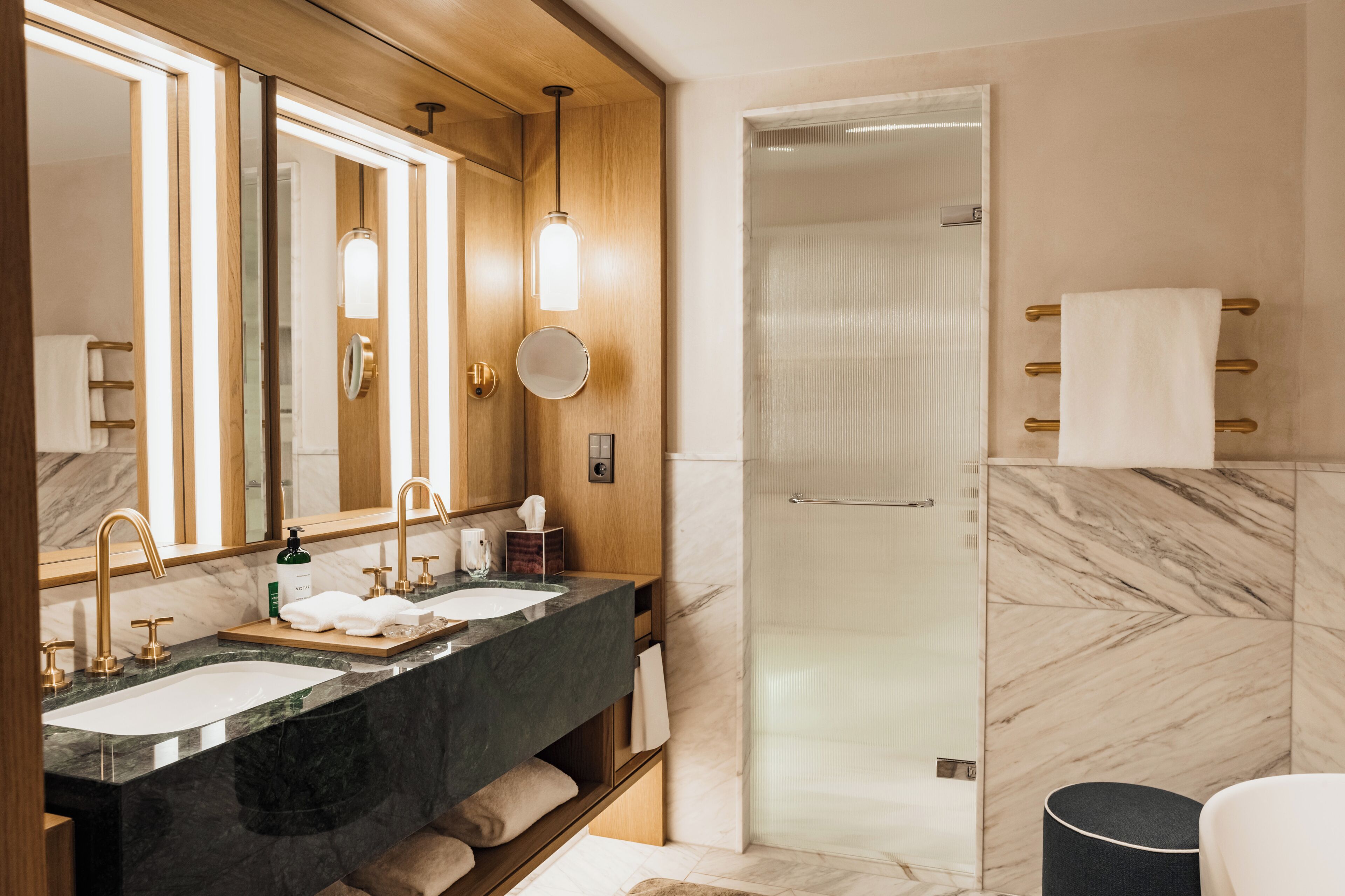 A modern bathroom with two sinks, a large mirror, a glass-enclosed shower, and marble walls.