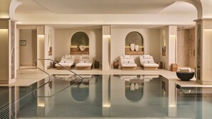 A modern spa with a large glass pool, two lounge chairs, and a shower area. - Rosewood Munich (Munich)