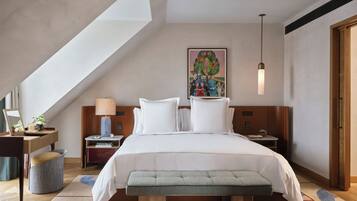 Una camera da letto moderna con soffitto spiovente, un letto grande, una panca, un comodino, una lampada e un quadro appeso al muro.