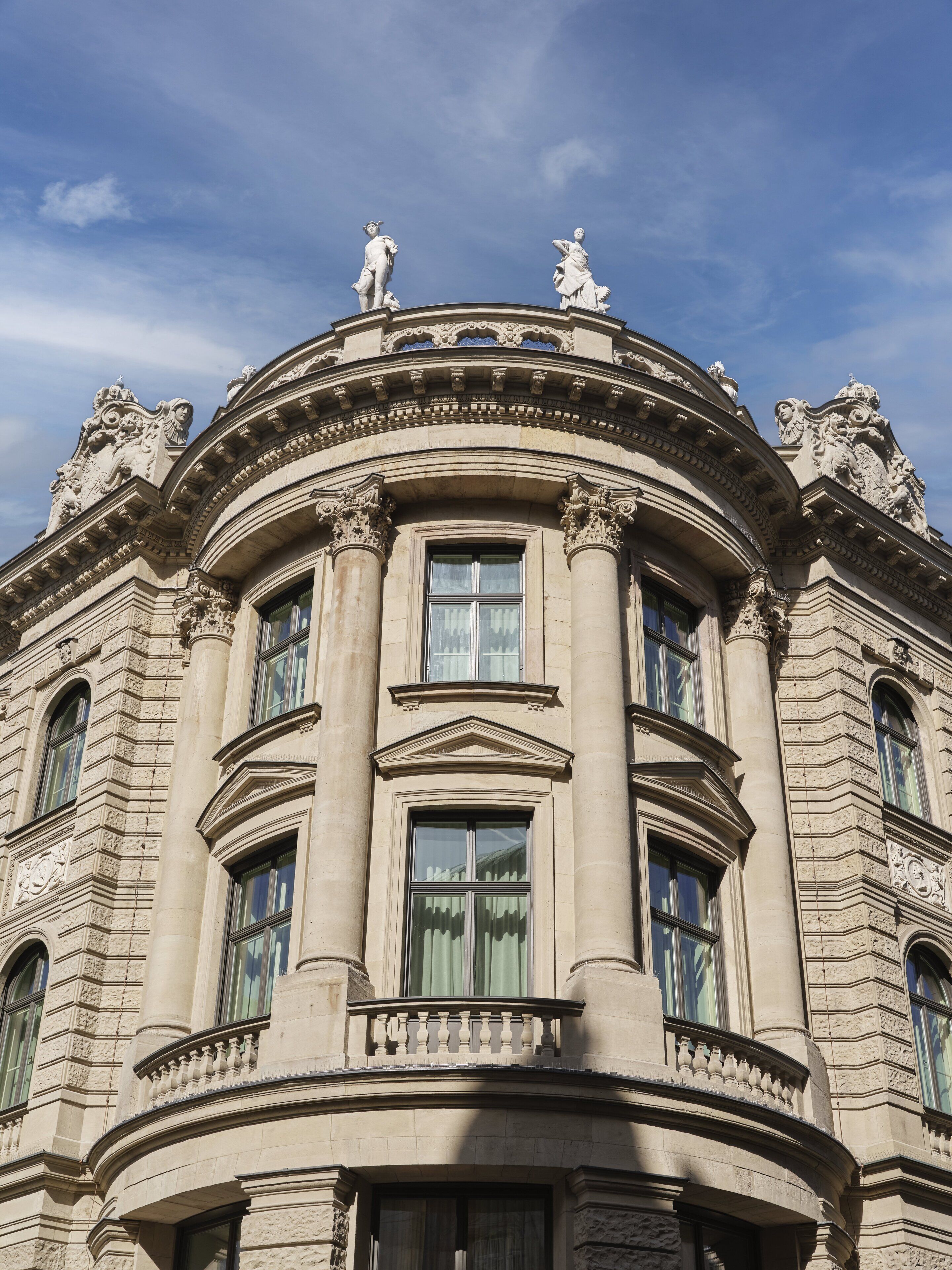 A classical building with ornate columns, large windows, and statues on the roof.