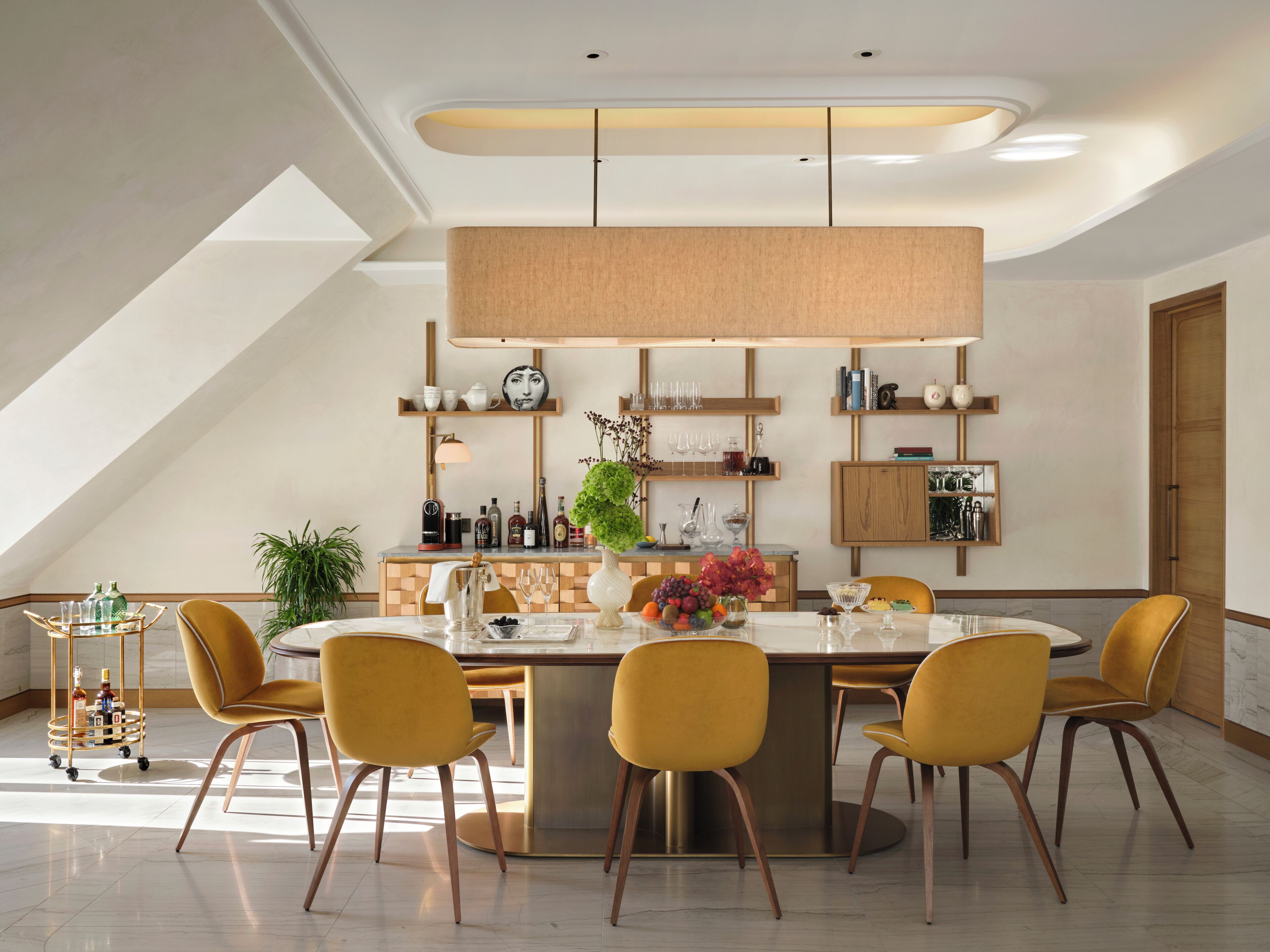 A modern dining area with a central island, yellow chairs, and a variety of tableware and decorative items.