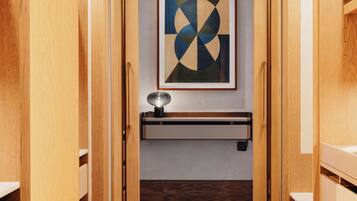 Un pasillo con taquillas de madera, una obra de arte abstracta enmarcada en la pared y un pequeño estante con una lámpara.
