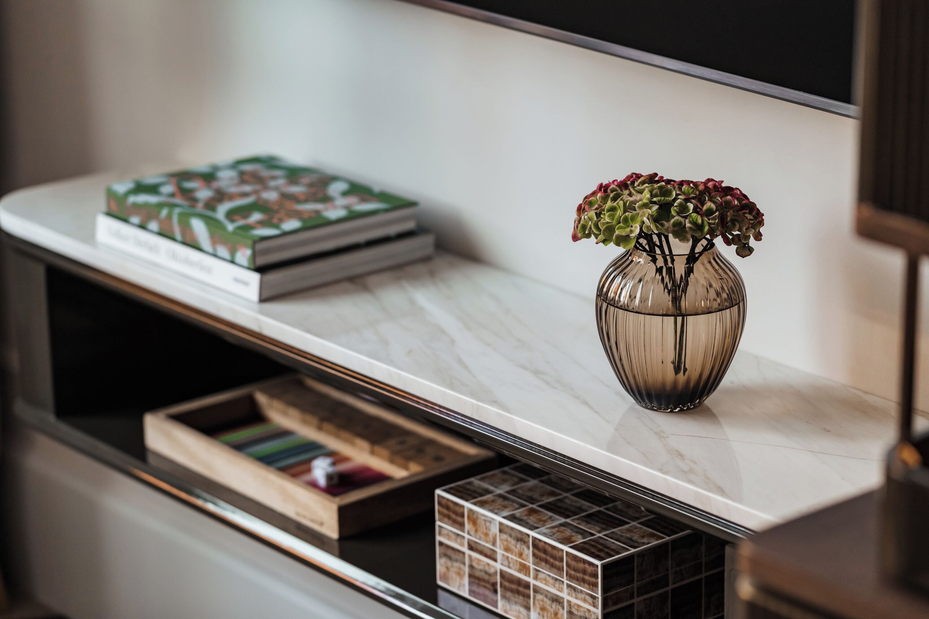 A marble countertop with a vase of flowers, a book, and a drawer.