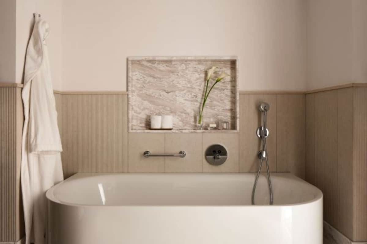 A modern bathroom with a freestanding bathtub, a towel rack, a wall-mounted shelf with toiletries, and a marble-like backsplash.