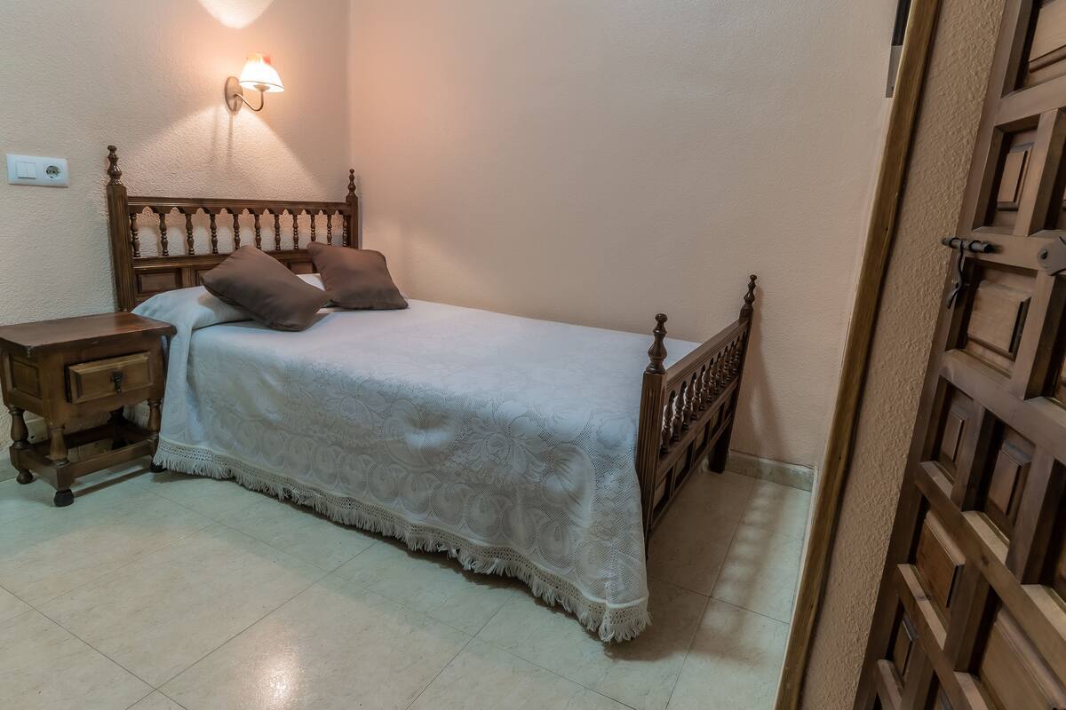 A bedroom with a wooden bed, a nightstand, a wall-mounted lamp, and a door with a wooden lattice design.