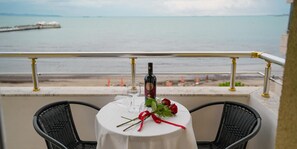 A table with a bottle and glass, two chairs, a bouquet of roses, and a view of the sea.
