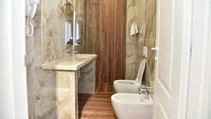 Un baño con pared de mármol, panel de madera, lavamanos, inodoro y bidé.